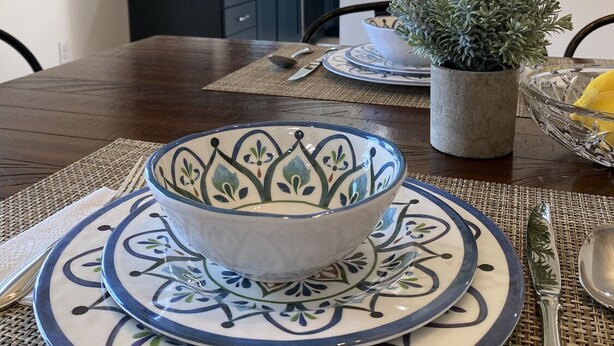 Una mesa de comedor adornada con un cuenco decorativo, platos y una planta en maceta.
