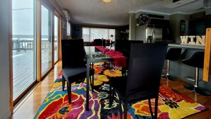 A dining area with a glass table, black chairs, and a colorful rug. - Shore Beats Work (East Jordan)