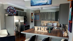 A modern kitchen with a central island, bar stools, stainless steel appliances, and a TV mounted on the wall. - Shore Beats Work (East Jordan)
