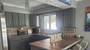 A modern kitchen with grey cabinets, a wooden island, and bar-style seating. - Shore Beats Work (East Jordan)