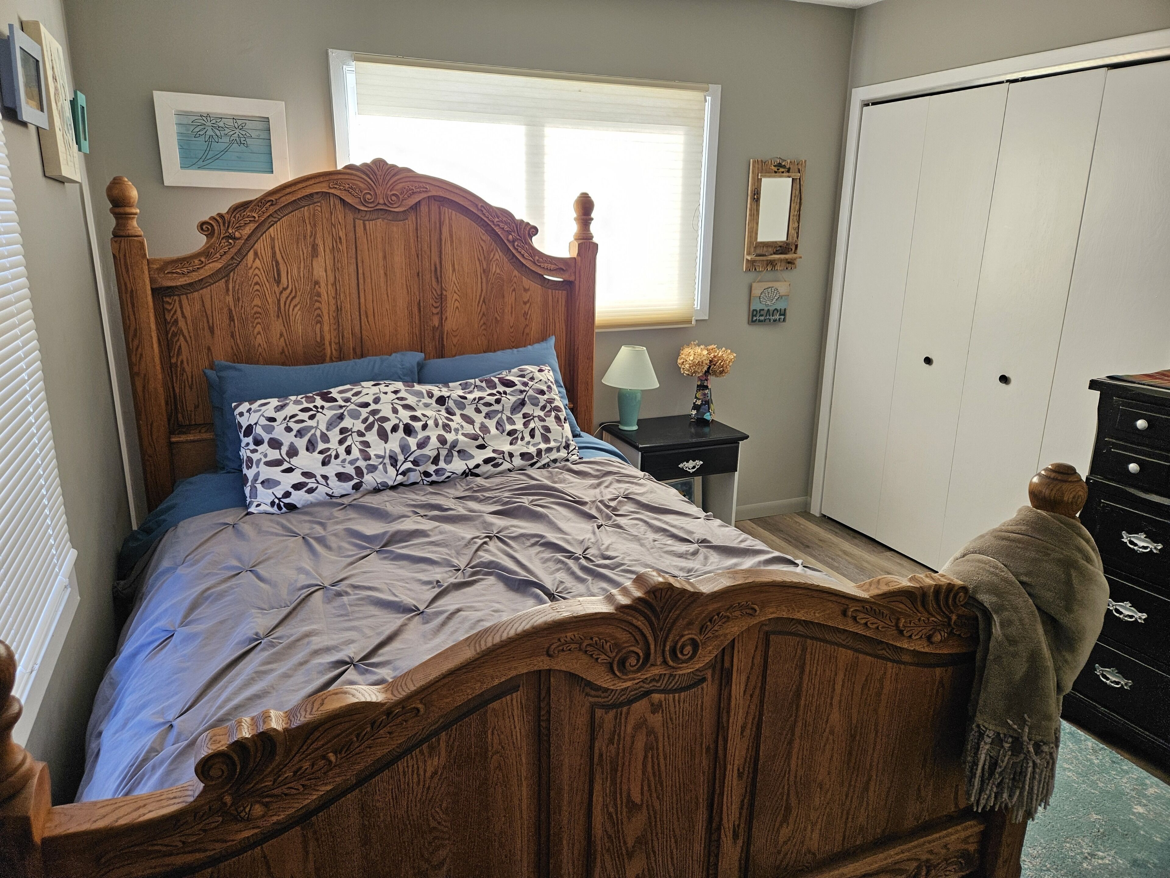 A bedroom with a wooden bed, a nightstand with a lamp, a dresser, and a wardrobe.