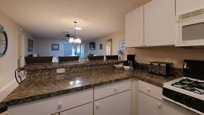 Una cocina con encimeras de granito, armarios blancos, estufa y microondas.