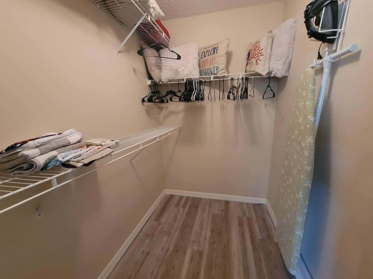 Een kleine, compacte kamer met een houten vloer, een witte radiator en een wandplank met opgevouwen kleding.