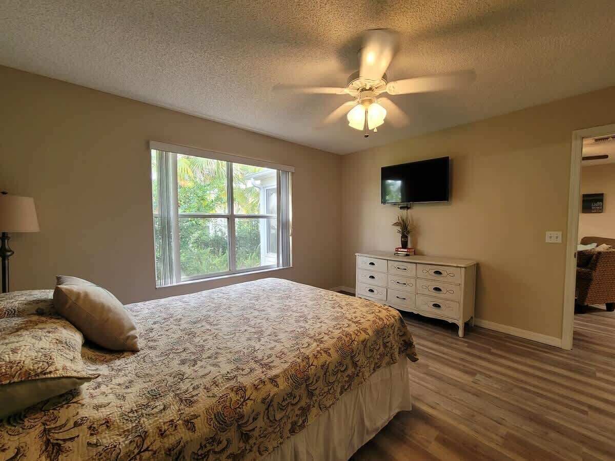 A bedroom with a large bed, a dresser, a ceiling fan, and a TV on the wall.