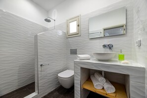 Een moderne badkamer met een douchecabine van glas, een wit toilet, een wastafel met spiegel erboven en een plank met handdoeken.