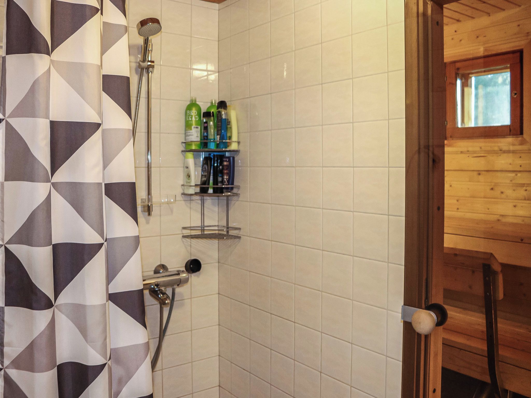 A shower area with a geometric-patterned shower curtain, a wall-mounted shelf with toiletries, and a wooden door with a window.