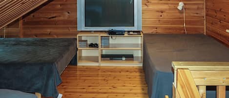 A small, wooden cabin with two beds, a television, and a shelf with various items.