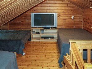 A small, wooden cabin with two beds, a television, and a shelf with various items.