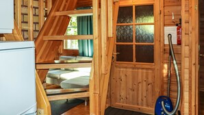 Interior de una cabaña de madera con una escalera, una puerta con ventanal y un aspirador.