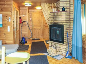 A wooden cabin interior with a fireplace, a vacuum cleaner, a sofa, and a dining table.