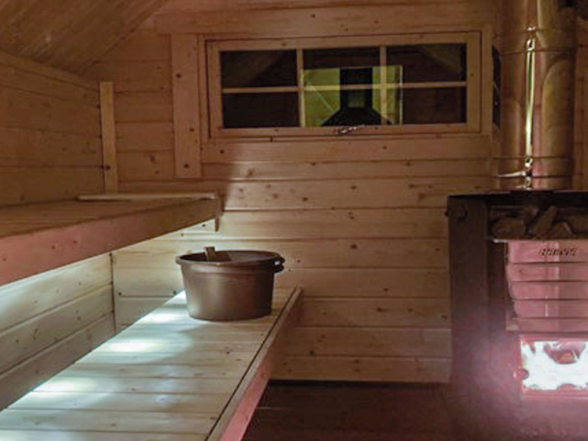 A cabin interior with a window, a wood-burning stove, and a pot on a shelf.