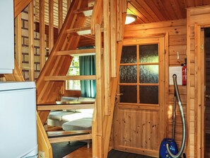 A wooden interior with a staircase, a door with windows, a vacuum cleaner, and a refrigerator.