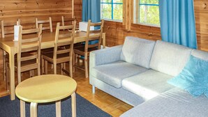 Interior de una cabaña de madera con una mesa de comedor, sillas, un sofá y ventanas grandes con cortinas azules.