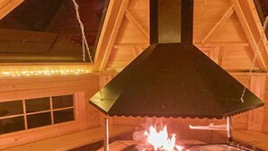 Una estufa de leña con chimenea, rodeada de vigas de madera y una ventana con persianas.