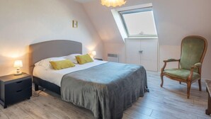 Ein Schlafzimmer mit einem Bett, Nachttischen, einem grünen Sessel, einem Oberlicht und einer Pendelleuchte.