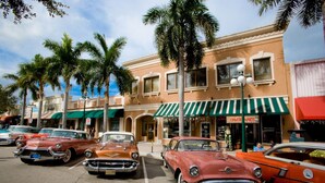A street lined with vintage cars parked in front of a building with a green awning and palm trees.