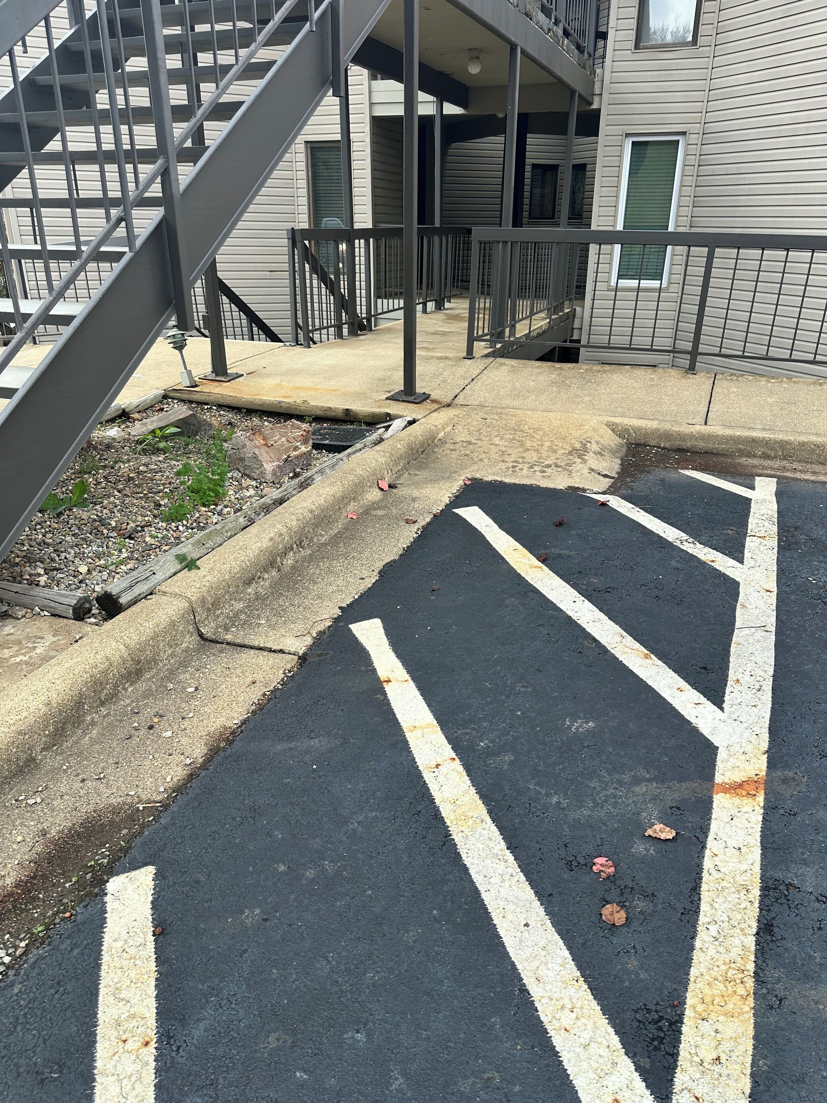A parking area with marked parking spaces, a concrete curb, and a metal staircase leading to a building with a balcony.