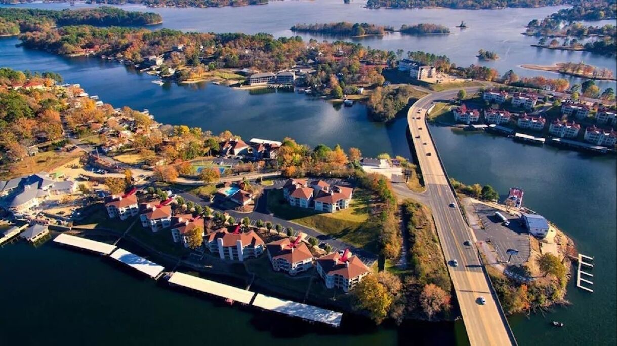 Eine Vogelperspektive auf einen Wohnbereich an einem See mit Häusern, einer Brücke und einem Steg.