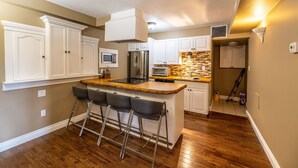 A modern kitchen with white cabinets, a wooden island with bar stools, stainless steel appliances, and a tiled backsplash. - The Elowen Suite (Drumheller)