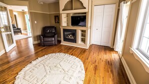 A living room with hardwood flooring, a fireplace, a television, and a door. - The Elowen Suite (Drumheller)