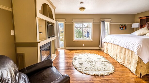 A bedroom with a bed, a fireplace, a window, and a view of the outdoors. - The Elowen Suite (Drumheller)