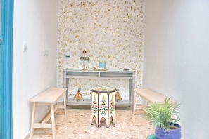 Cozy room with a simple layout, featuring a round table and two benches, a console above, and a potted plant.