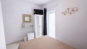 A bedroom with a bed, a wardrobe, a small bedside table, a mirror, and a wall-mounted light fixture.