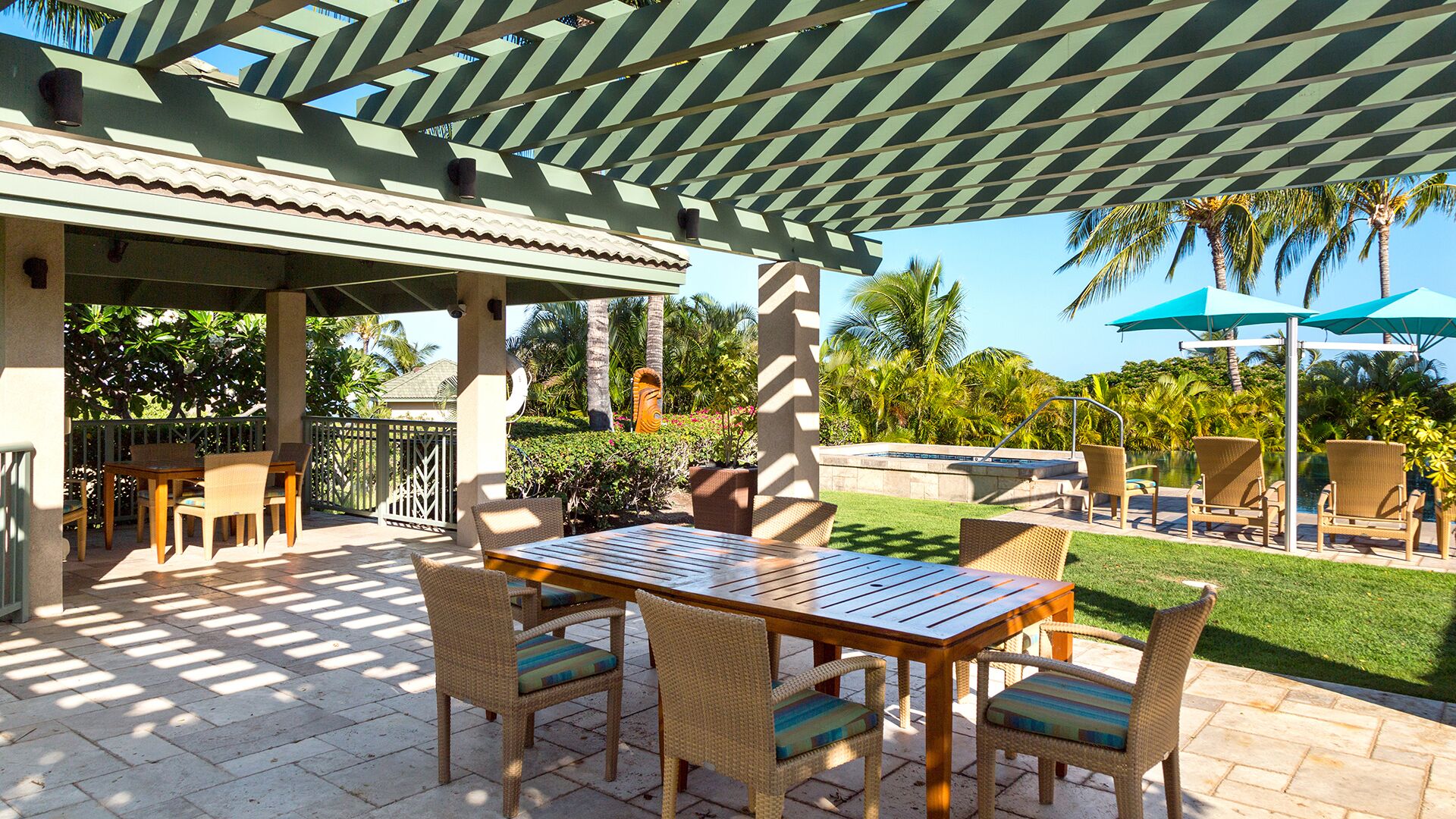 An outdoor patio with a covered seating area, a pool, and lush greenery.