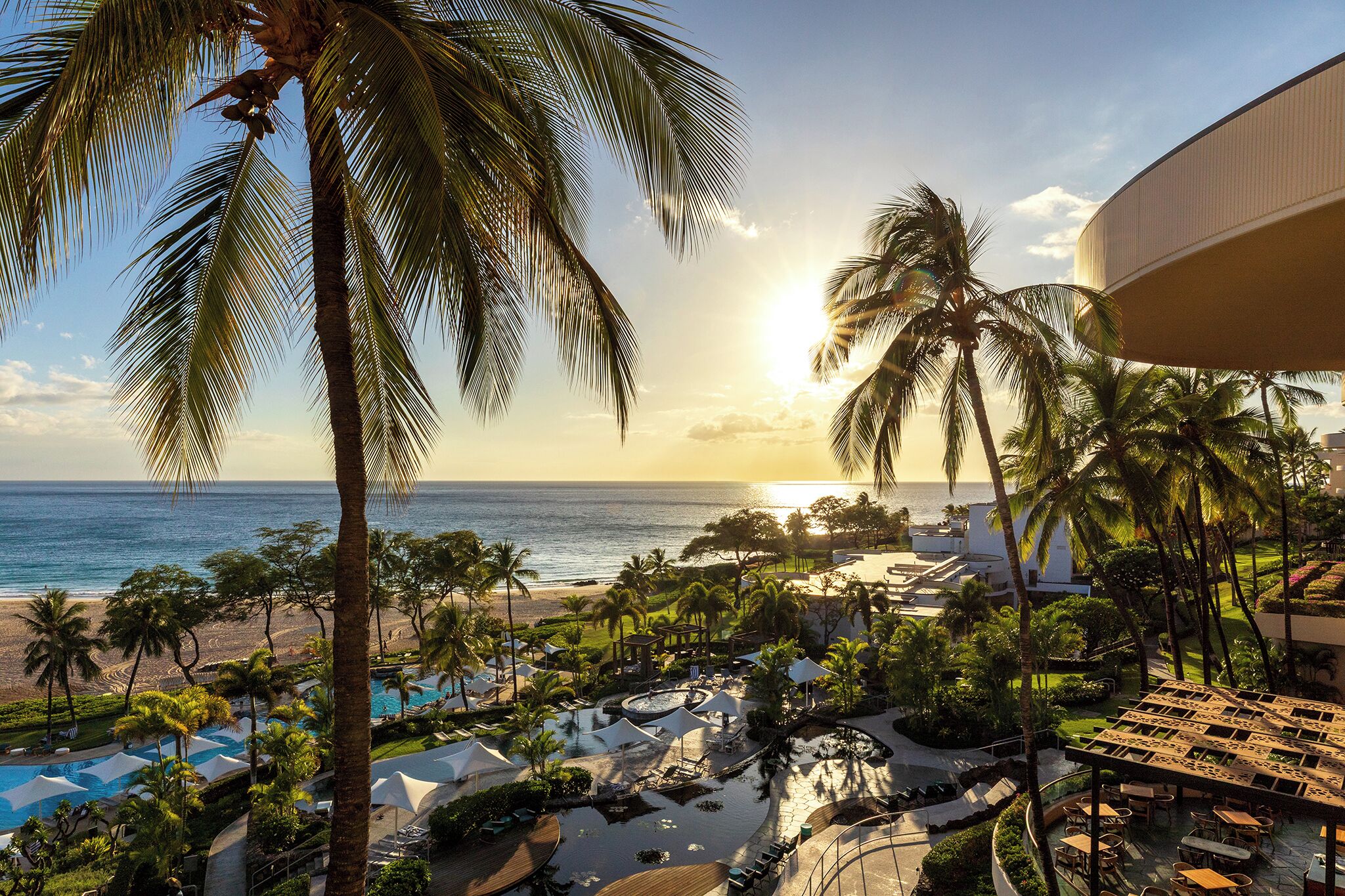 Een resort met een zwembad, palmbomen en uitzicht op de oceaan bij zonsondergang.