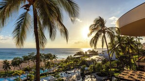 Un resort con piscina, palmeras y vistas al océano al atardecer.