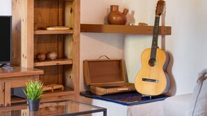 Ein Wohnzimmer mit einem Glastisch, einem Blumentopf, einer Gitarre, Holzregalen und einem weißen Sofa.