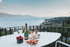 A table with a bottle of wine, glasses, strawberries, and a plate of food on a balcony with a scenic view.