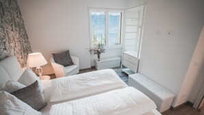 Ein Schlafzimmer mit einem Bett, Nachttischen, einem Sessel, einer Lampe, einem Fenster mit Blick und einer Kommode.