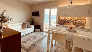 Ein modernes Wohnzimmer mit einer Couch, einem Couchtisch und einem Fernseher. Es gibt eine Küchenzeile mit einer gefliesten Spritzschutzwand und einem Esstisch.