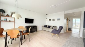A modern living room with a dining area, a flat-screen TV, and a sofa.
