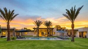 Et moderne hus med swimmingpool, palmer og en solnedgang.