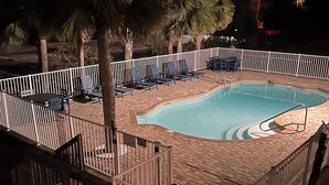 A swimming pool with a white fence, lounge chairs, and palm trees. - 2 Br 1 Bath Condo in Gulfshores, AL, 2 min walk to the Beach, Pool and Fishing (Gulf Shores)