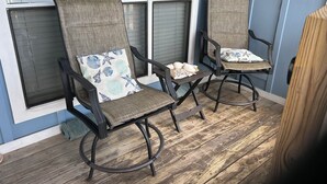 Two wicker chairs with starfish pillows, a small table with a bowl and a candle, and a wooden floor. - 2 Br 1 Bath Condo in Gulfshores, AL, 2 min walk to the Beach, Pool and Fishing (Gulf Shores)