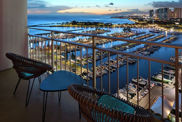 A balcony with wicker furniture overlooking a marina with numerous boats and a cityscape in the background.