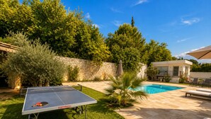 Un espace aménagé au bord de la piscine, comprenant une table de ping-pong, un mur en pierre et la piscine elle-même.