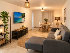 A modern living room with a grey sofa, a TV displaying a beach scene, a dining area with a table and chairs, and a floor lamp. - Luxury villa in Aix en Provence, with 2 private accommodation (Aix-en-Provence)