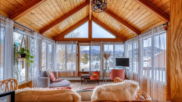 A cozy, well-lit room with wooden beams, large windows, a comfortable seating area, and a television.