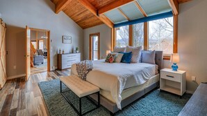 A bedroom with a large bed, a bench, a nightstand, and a window with blinds.