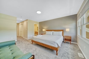 A bedroom with a large bed, a green chair, a nightstand, and a window.