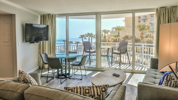 A modern living room with a large balcony, a flat-screen TV, a dining area, and a sofa. - LUXURY OCEANFRONT 2BR Condo, Pool & Hot Tub, Game Rooms, Great Views (Daytona Beach Shores)