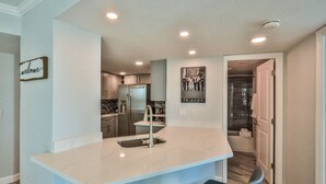 A modern kitchen with a marble countertop, stainless steel appliances, and a "welcome" sign. - LUXURY OCEANFRONT 2BR Condo, Pool & Hot Tub, Game Rooms, Great Views (Daytona Beach Shores)