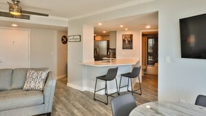 A modern living room with a grey sofa, a coffee table, and a bar area with two bar stools. - LUXURY OCEANFRONT 2BR Condo, Pool & Hot Tub, Game Rooms, Great Views (Daytona Beach Shores)