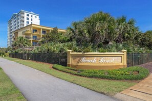 Señal de Beach Resort con un camino pavimentado y un edificio de varios pisos al fondo.