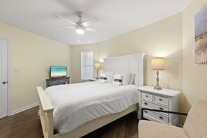 Ein Schlafzimmer mit einem Bett, einem Nachttisch, einer Lampe, einem Fernseher und einem Deckenventilator.
