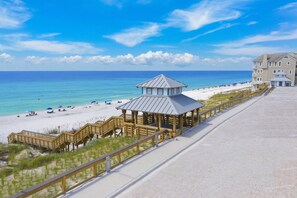 A beach with a wooden boardwalk leading to a gazebo-like structure, a sandy beach, and a building in the background. - Amalfi Coast 411A - Gulf Views, Heated Community Pool, Easy Walk to the Beach! (Miramar Beach)